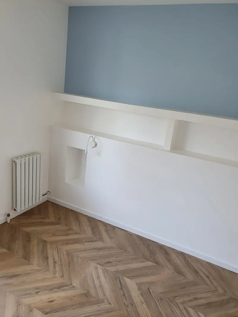 Chambre au mur bleu avec radiateur et parquet chevron