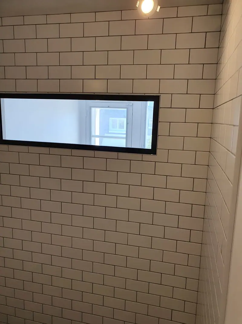 Mur de salle d'eau en faïence métro beige avec fenêtre encadrée de noir