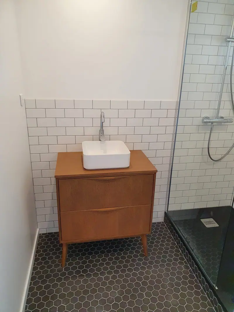 Vasque posée sur un meuble en bois dans une salle d'eau en faïence métro