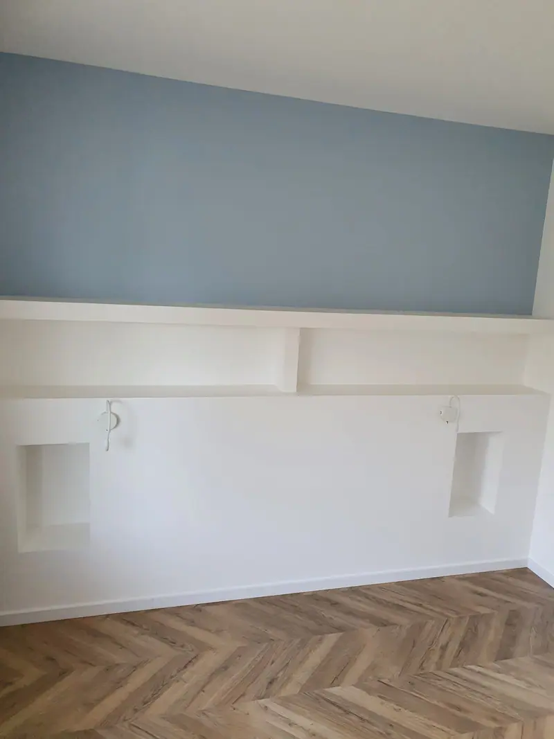 Mur peint en bleu avec niches de rangement intégrées au-dessus du parquet