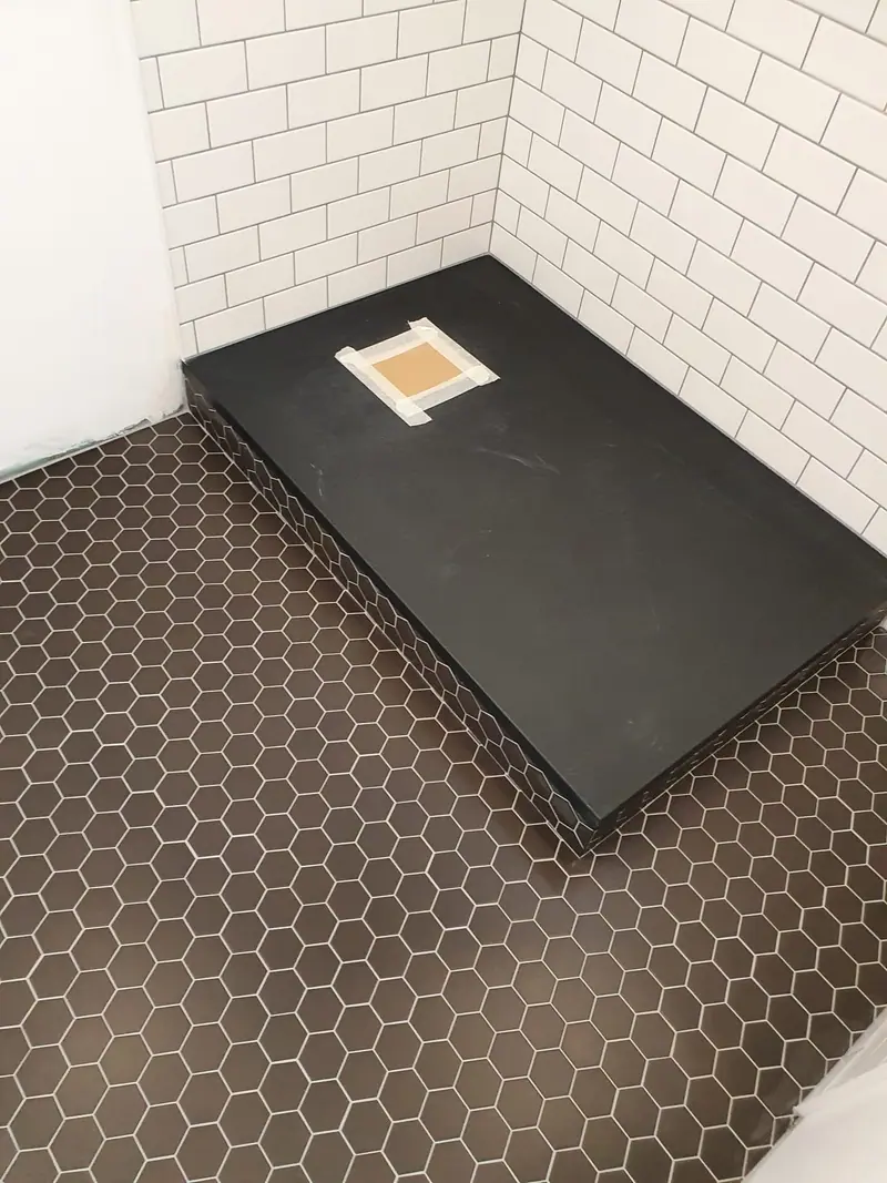 Receveur de douche noir extra-plat posé sur un sol en carreaux hexagonaux